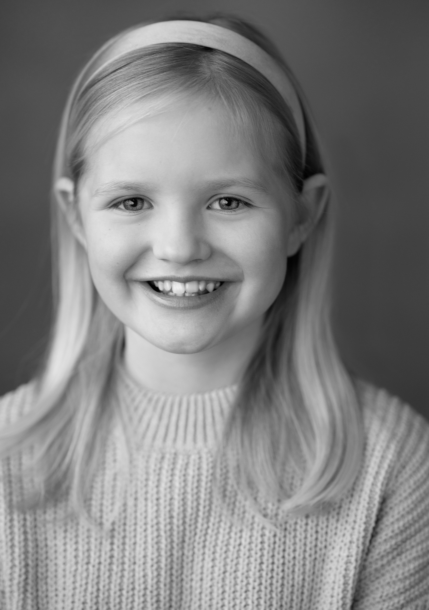 girl with a band in her hair and a long blond hair smiles towards the camera